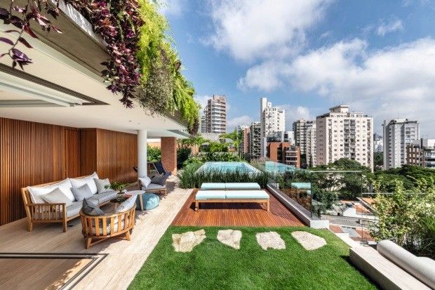 Cobertura residencial sofisticada em contexto urbano de São Paulo, integrando um exuberante jardim vertical com espécies tropicais pendentes como tradescântias roxas e ripsális que descem pelas platibandas, criando uma cortina vegetal que suaviza a arquitetura contemporânea. O terraço combina deck de madeira cumaru, gramado com pisantes de pedra natural irregular e piscina elevada com borda infinita que emoldura a vista da cidade, enquanto o mobiliário em madeira teca com almofadas em tons neutr, estilo Moderno, Tropical, elementos jardim vertical exuberante em parede e platibanda, piscina elevada com borda infinita e revestimento em pastilha azul, deck de madeira cumaru, pisantes de pedra irregular sobre gramado, mobiliário de madeira teca com estofados em tons neutros, daybed junto à piscina, guarda-corpo de vidro temperado transparente, painel ripado de madeira cumaru, pufe azul turquesa, pedras naturais ornamentais sobre gramado, cobertura parcial em laje com vegetação pendente, plantas Tradescântia-roxa, Lambari-roxo, Palmeira-areca, Ripsális, Singônio, Peperômia, Grama-esmeralda, Unha-de-gato, Helicônia, Filodendro, Jiboia, Samambaia, ambiente sofisticado, moderno, relaxante, localização varanda, piscina, jardim, área grande, estruturas banco, iluminacao, cores verde-escuro, verde-claro, roxo, marrom-madeira, branco, cinza, azul-turquesa, bege, piso deck, grama, pisantes, privacidade muro_verde, água piscina